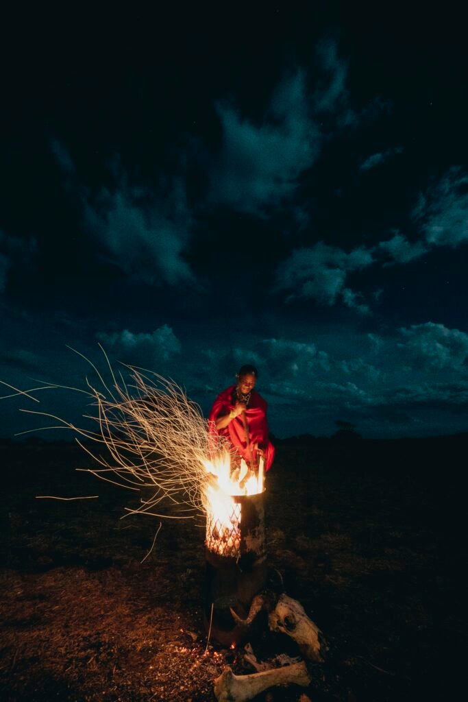 Maasai man standing by fire at night in the Serengeti during a cultural ceremony photographed for Melia Serengeti.